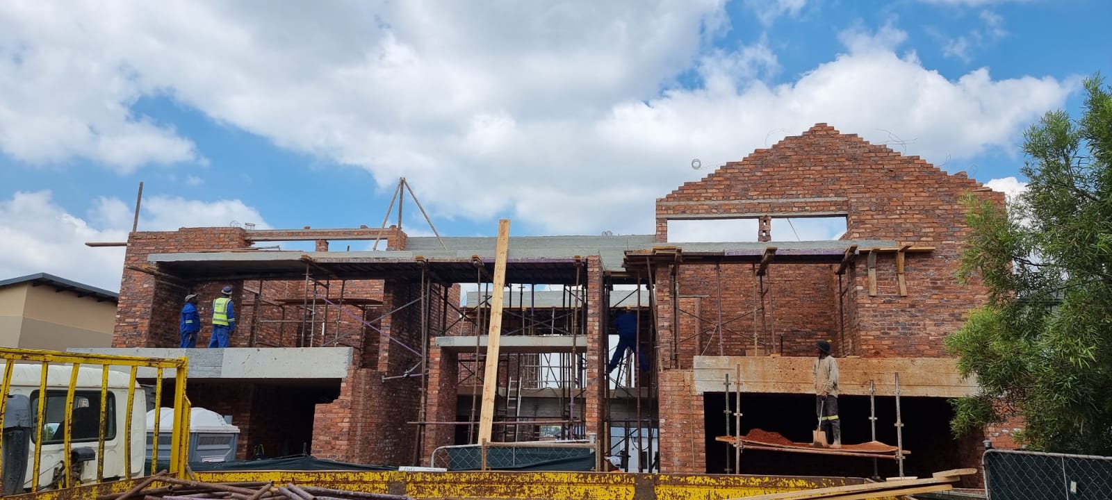 Two-storey brick shell of a home under construction with roof trusses going up
