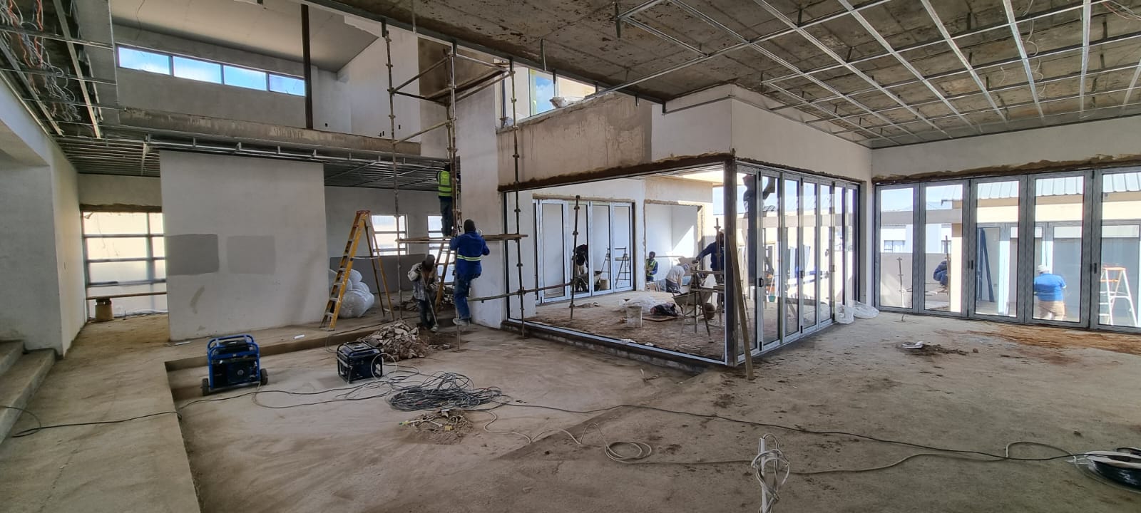 Open-plan living area mid-build with folding glass doors and tiling underway